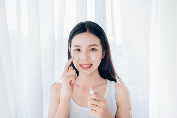 Woman smiling in front of white background and applying acne treatment to face