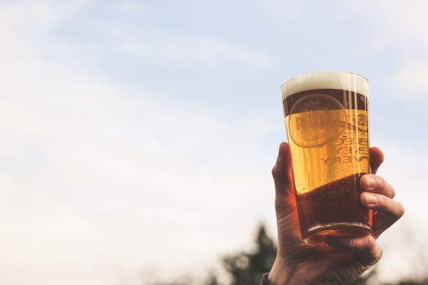 Hand holding a glass of beer in the air in front of blue sky