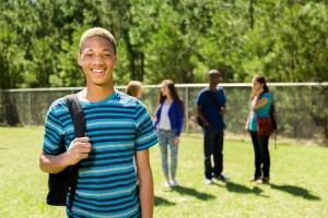 Boy in blue striped shirt smiling outside in front of a group of peers