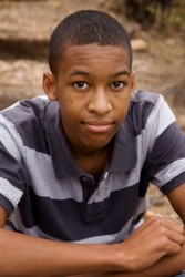 Boy in purple striped polo sitting on the ground, looking up at the camera