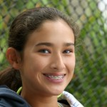 Girl smiling outside in front of a wire fence