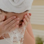 Woman with hair in towel, leaning over the sink, splashing water onto her face