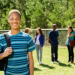 Boy in a blue striped shirt, smiling outside in front of group of peers