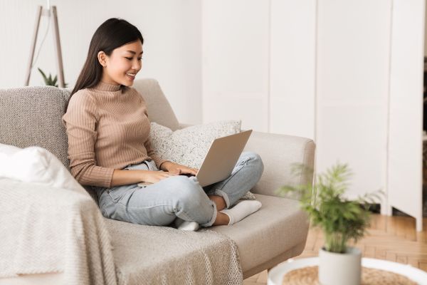 Woman sitting cross legged on couch, smiling at laptop